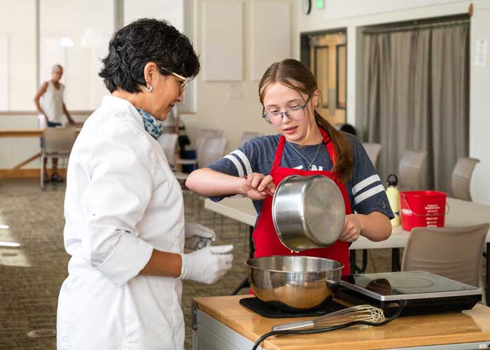 Kitchen-GreatRoom-2022 People cooking in BARN kitchen with Great Room visible behind them