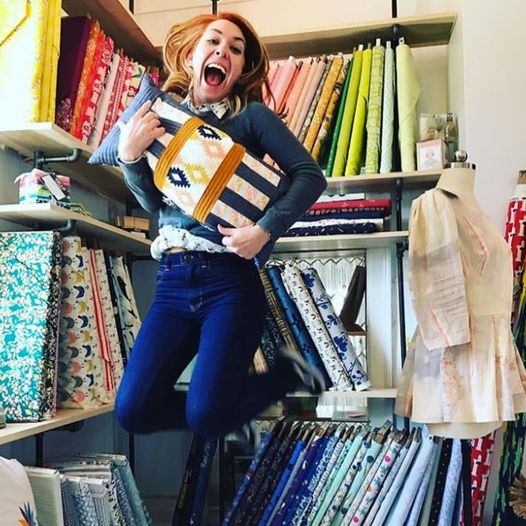 Lauren Taylor jumping in the air in front of a wall filled with colorful fabric