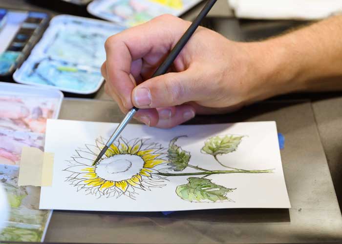 Person working on a watercolor painting of a sunflower at the BARN Bazaar