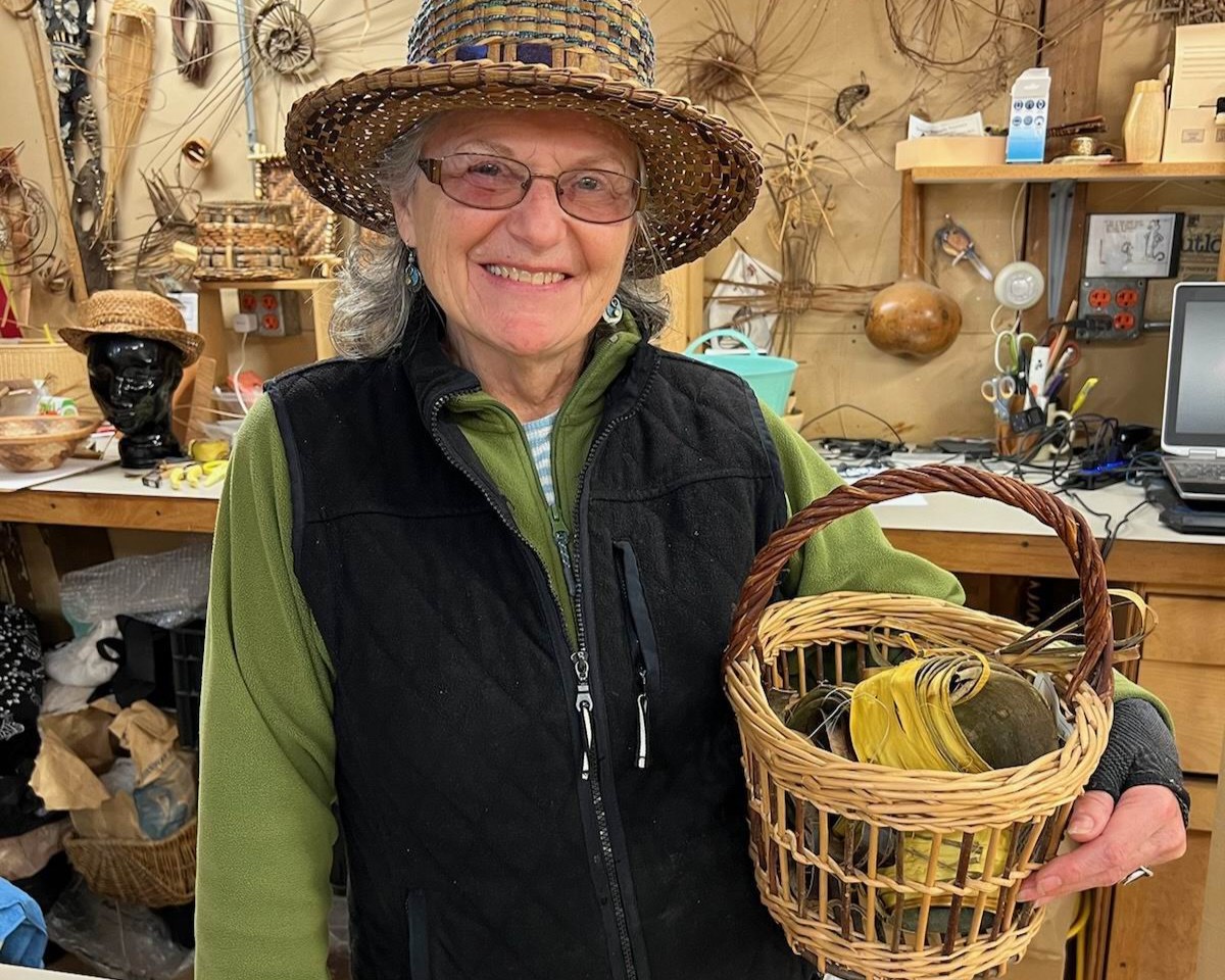 Photo of Judy Z holding a basket and wearing a woven hat